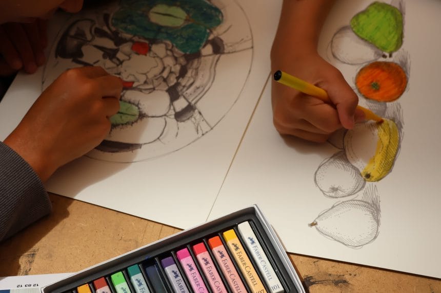 Cutie de creioane colorate Faber-Castell, lângă un desen în creion cu fructe, la un atelier din cadrul Nopții Muzeelor, Muzeul de Artă Constanța