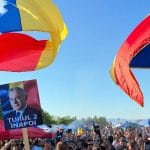 Ilustrație generată cu AI: mulțime la un miting cu steaguri românești și afiș cu mesajul „Turul 2 înapoi”